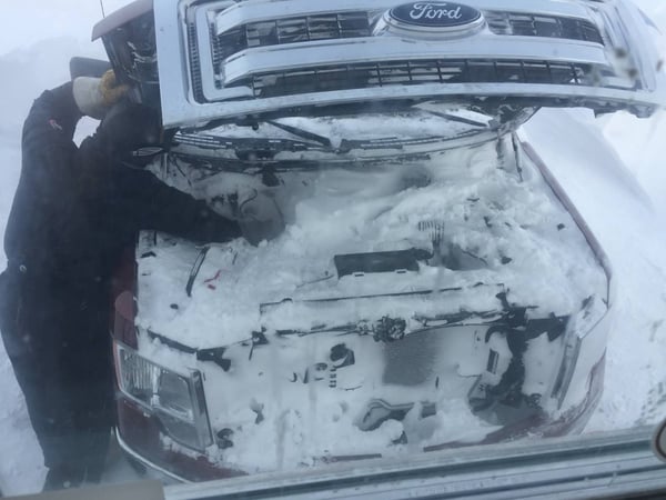 A photo showing people digging snow out of the engine bay of a truck