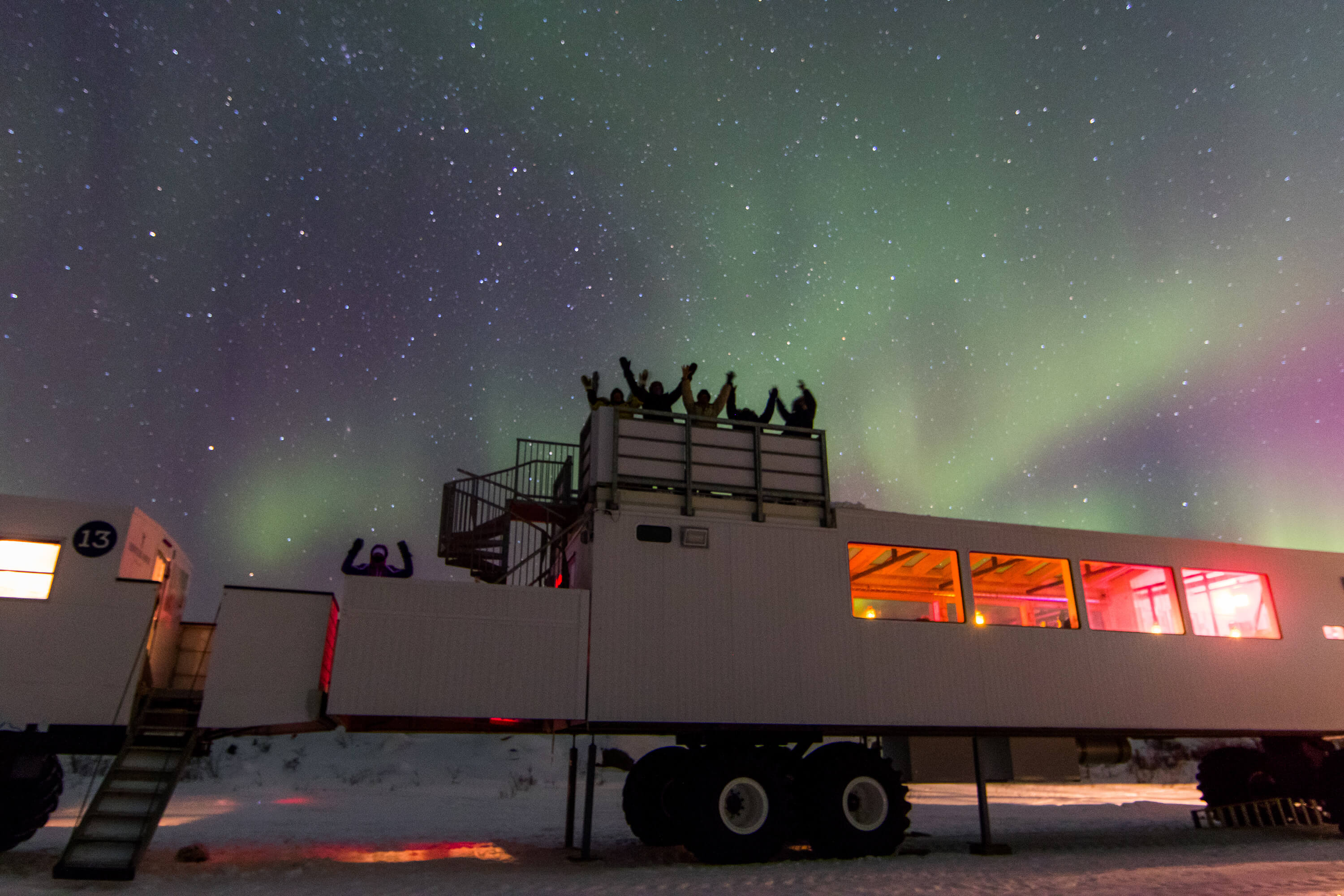 Guests beneath the northern lights on Thanadelthur Lounge's rooftop observation deck in Churchill, Canada.