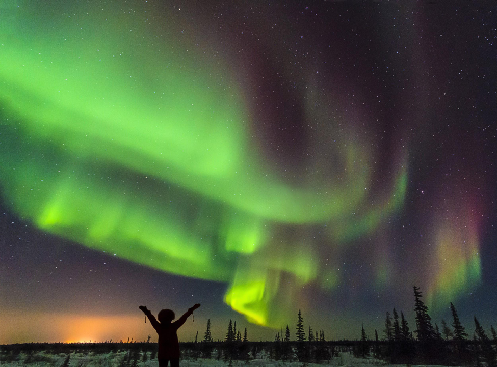 A person stands below an active northern lights display