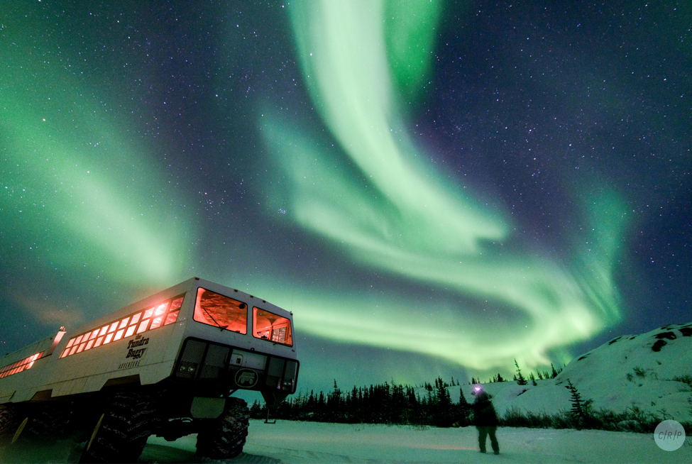 A guest experiences the northern lights as a buggy rests on the tundra nearby