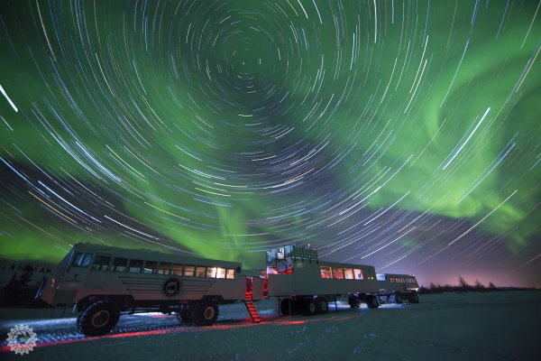 A timelapse photograph of the northern lights with a Tundra Buggy&reg; and the lounge car from our Lodge.